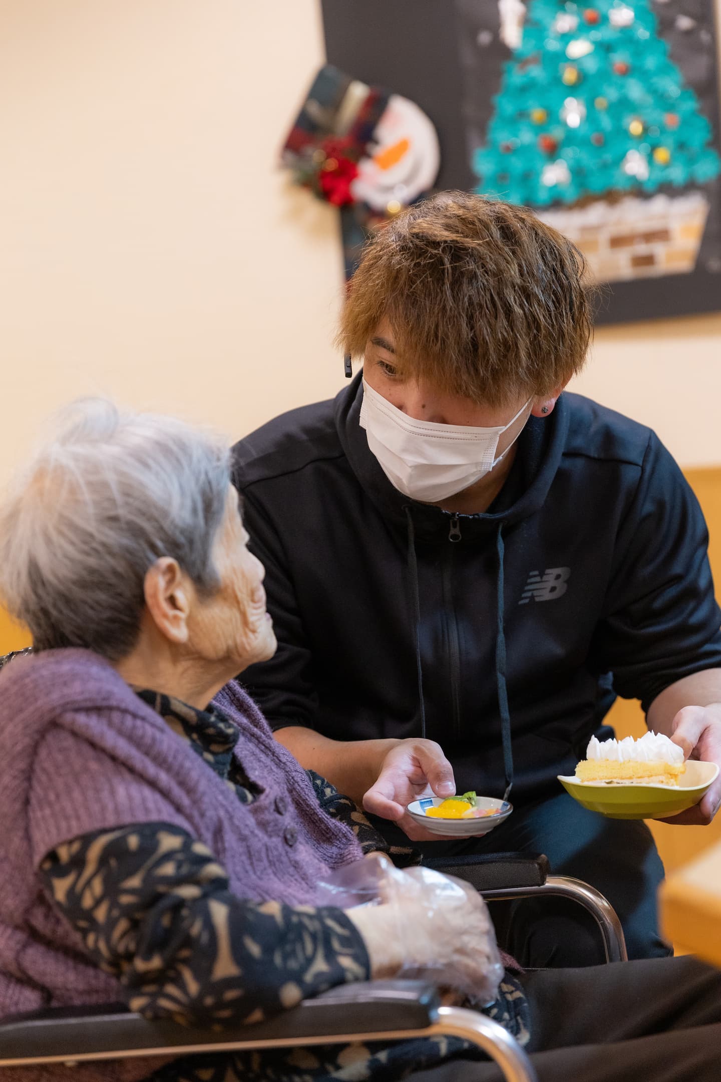 スタッフが入居者に食事を提供する様子。クリスマスの装飾が見える共用部での温かい交流風景。